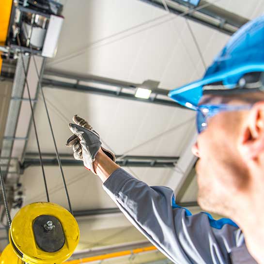 Worker in a hard hat and safety glasses pointing up at a crane hoist
