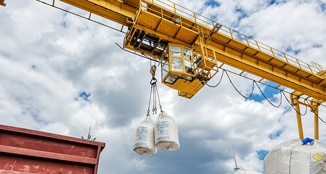 Yellow gantry crane lifting two bulk bags outdoors